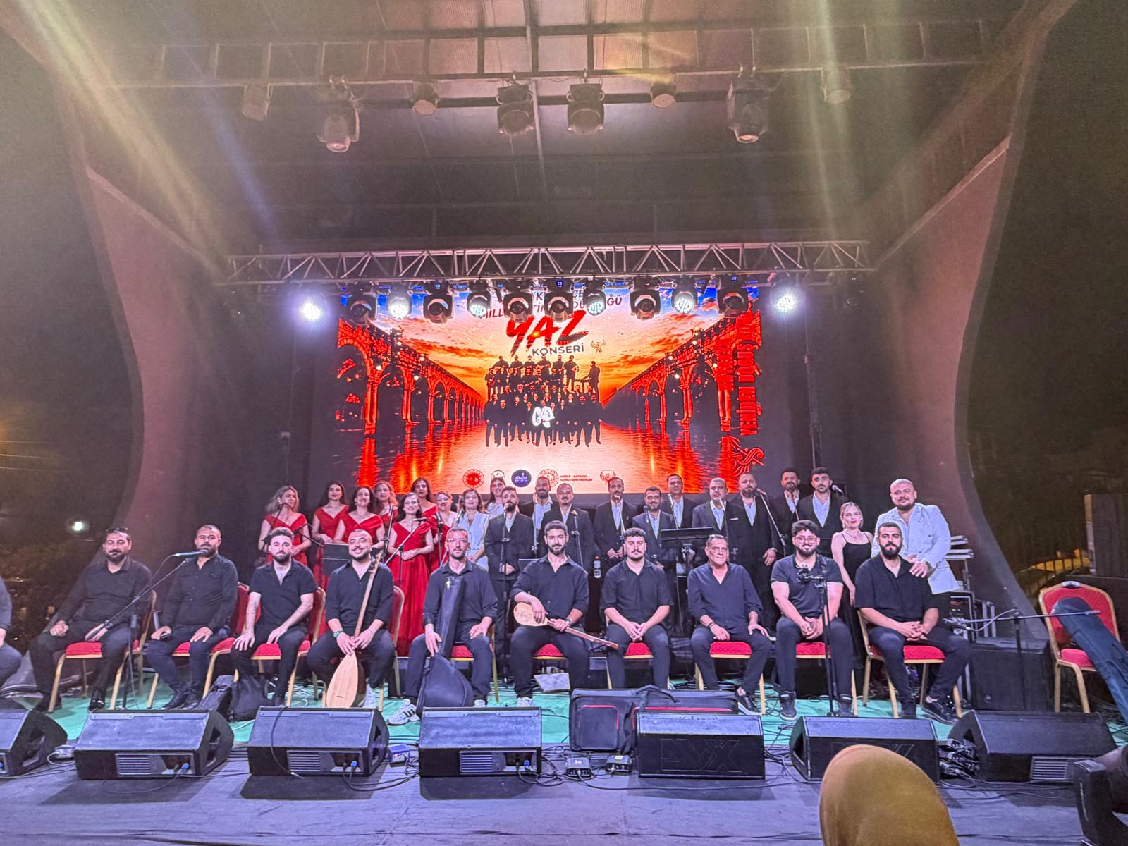 Konser sahnesinde koro ve enstrümanlarıyla müzisyenlerin toplu fotoğrafı